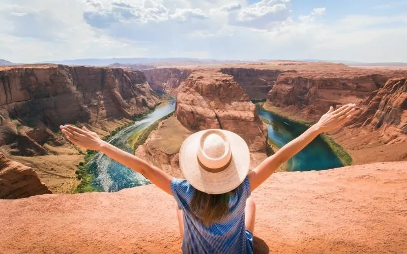 Woman in sunhat with outstretched arm in foreground, Grand Canyon in background